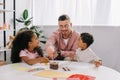 smiling caucasian teacher in eyeglasses and african american kids drawing pictures with paints together Royalty Free Stock Photo