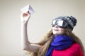 Smiling Caucasian Teenage Girl in Flying Gear And Warm Hat Launching Origami Paper Plane Over Beige Background Royalty Free Stock Photo