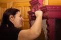 Smiling Caucasian woman coloring wooden ornamented cupboard in red with large paint brush with doors in background