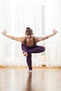 Smiling Caucasian Woman Practicing Yoga Asana Indoors in Front of Big Sunny Window. Standing on One Foot With Hands Stretched Out Royalty Free Stock Photo