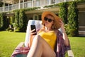 Smiling caucasian woman sitting in sunny garden wearing sunhat and sunglasses using smartphone Royalty Free Stock Photo