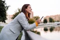 smiling caucasian woman wearing yellow pullover and grey coat using mobile phone device outdoors in park during sunset. Technology Royalty Free Stock Photo