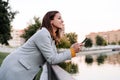 smiling caucasian woman wearing yellow pullover and grey coat using mobile phone device outdoors in park during sunset. Technology Royalty Free Stock Photo