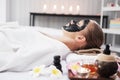 Smiling Caucasian woman in white is laying on bed and black facial mask on face for treatment skine care in spa Royalty Free Stock Photo