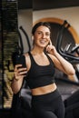 Smiling caucasian young woman listens to music through wireless headphones on smartphone in gym. Royalty Free Stock Photo