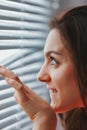 Smiling but cautious woman peering through blinds Royalty Free Stock Photo