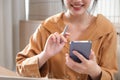 Smiling and charming Asian woman sit at her desk with a smartphone playing social media applications and transacting at her desk Royalty Free Stock Photo