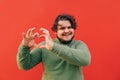 Smiling charming young obese bearded guy is expressing a love sigh gesture with his hands, being happy and romantic, looking cute Royalty Free Stock Photo