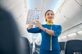 Smiling cheerful air hostess in blue uniform showing to passenger safety information Royalty Free Stock Photo