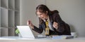 Smiling and cheerful Asian businesswoman looking at her laptop screen, raising her hand, rejoicing and celebrating her Royalty Free Stock Photo