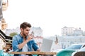 Smiling cheerful casual man using laptop outdoors and drinking coffee Royalty Free Stock Photo