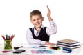 Smiling cheerful excellent pupil with hand up sitting at the table on the white background