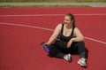 A smiling, cheerful, full-bodied woman with a bottle of water sits on the stadium floor. Royalty Free Stock Photo