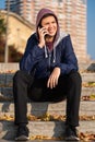 Smiling cheerful teenage boy talking on mobile phone sitting on stairs outdoors in the city Royalty Free Stock Photo