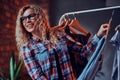 Smiling cheerful woman in glasses and checkered shirt chooses clothes in butique for her holidays