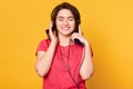 Smiling cheerful young female standing isolated over yellow background in studio, closing her eyes while listening to music, Royalty Free Stock Photo