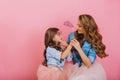 Smiling cheerful young mother looking with love at her long-haired daughter wearing purple carnival mask. Adorable Royalty Free Stock Photo