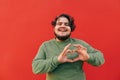 Smiling cheerful young obese hispanic man is expressing a love sigh gesture with his hands, feeling happy and romantic, looking at Royalty Free Stock Photo