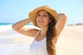 Smiling cheerful young woman with straw hat enjoying wind on the beach