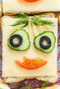 Smiling cheese sandwich with face from cucumbers, tomato, olives and dill