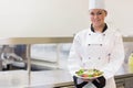 Female chef in uniform holding plate of colorful salad on stainless steel countertop, copy space Royalty Free Stock Photo