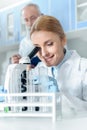 Smiling chemist in white coat working with microscope and reagents while in chemical lab