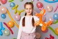 Smiling child. Birthday party. Delighted satisfied little girl with braids standing against gray wall decorated with colorful Royalty Free Stock Photo
