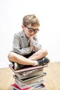 Smiling child with bookworm eyeglasses seated on pile of books