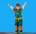 Smiling child boy in helmet and toolbelt raised hands. Little repairman with tools for building. Kid in builder uniform Royalty Free Stock Photo