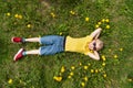 Smiling child lies on grass in dandelions flower field and dreaming. Boy puts his hands behind his head. Top view Royalty Free Stock Photo