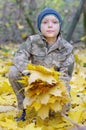 Smiling child playing with fallen autumn leaves. Boy holding bunch of maple leaves in the forest Royalty Free Stock Photo