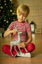 Smiling child in a red Santa Claus hat playing with new year silver deer with on the background of the christmas tree