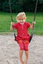 Smiling child sitting on swing. Happy kid playing in park. Girl swinging at playground in summer Royalty Free Stock Photo