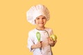 Smiling child in white chef uniform,holding a cabbage and a whisk in his hands. Cheerful yellow background Royalty Free Stock Photo