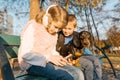 Smiling children boy and girl sitting on bench in the park with dog dachshund, children best friends laugh, look at the smartphone