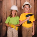 Smiling children in hard hats with construction tools on wooden