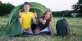 Smiling children lying in the tent in the park showing thumb up gesture. Camping, tourism and teenagers activity or leisure