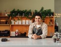 Smiling coffee shop owner in apron leaning a counter. Middle eastern bartender looking at camera