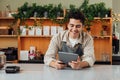 Smiling coffee shop owner at the counter with digital tablet. Male bartender in an apron leaning counter looking at a portable