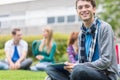 Smiling college boy using tablet PC with students in park