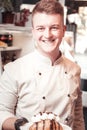 A smiling confectioner holding a plate with a dessert