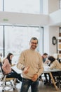 Smiling confident businessman giving thumbs up in busy office environment.