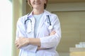Smiling confident female doctor in white workwear with stethoscope, standing with arms crossed in clinic hospital. Professional Royalty Free Stock Photo