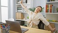 Smiling, confident hispanic woman stretching her tired arms while working online on her laptop at the office Royalty Free Stock Photo