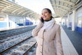 Smiling confident woman commuter talking on mobile phone, standing on the platform of a railway station Royalty Free Stock Photo