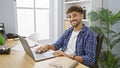 Smiling, confident young arab man joyously working on his laptop at the office, exuding positivity as the successful manager that Royalty Free Stock Photo