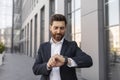 Smiling confident young european guy boss with beard in suit look time at clock, waiting for meeting Royalty Free Stock Photo