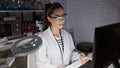 Smiling, confident young hispanic woman scientist, beautiful in her glasses, enjoying her work on the computer at the lab Royalty Free Stock Photo