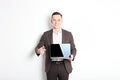 Smiling confident young man, no tie, holding grey laptop device and typing while standing against solid white wall. Wireless inter Royalty Free Stock Photo