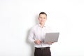 Smiling confident young man, no tie, holding grey laptop device and typing while standing against solid white wall. Wireless inter Royalty Free Stock Photo